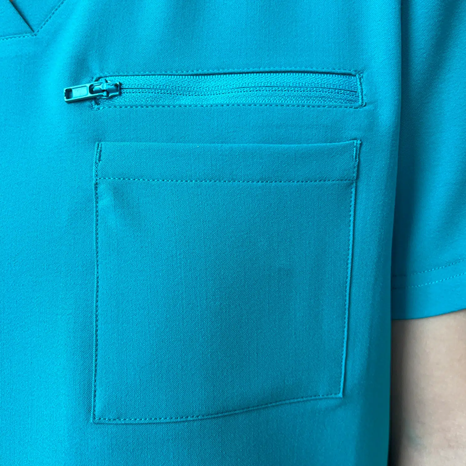 Front view of teal women’s surgical gown top with a V-neck and zippered pocket, designed for healthcare use.