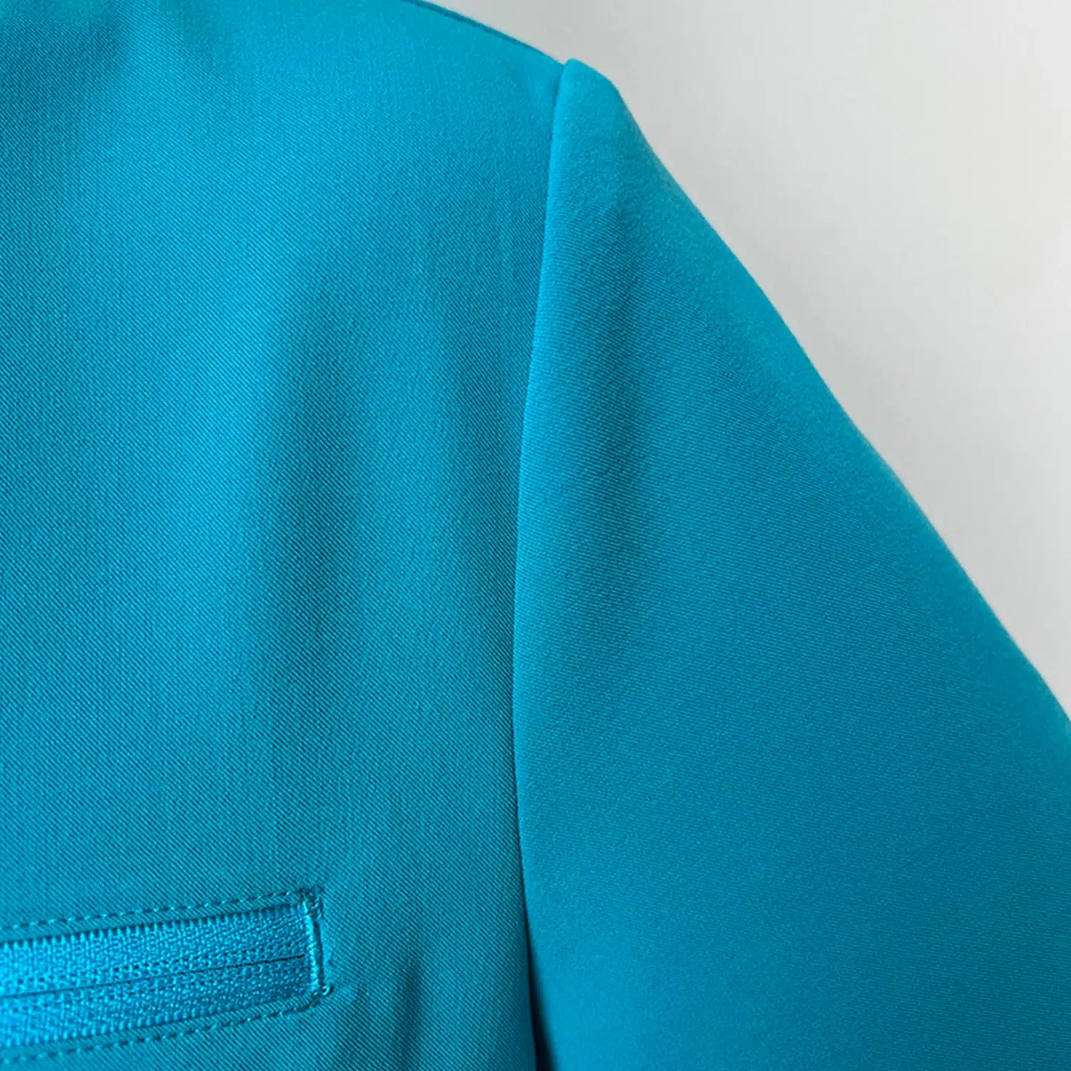 Side view of teal women’s surgical gown top with zippered pocket and short sleeves, designed for healthcare workers.